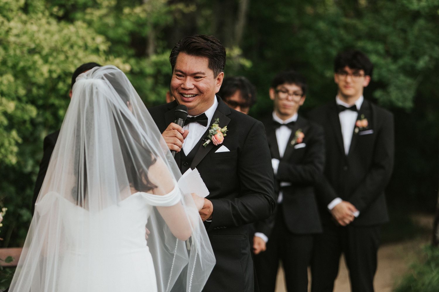 Wedding party members pose for formal photos outdoors with trees in background.