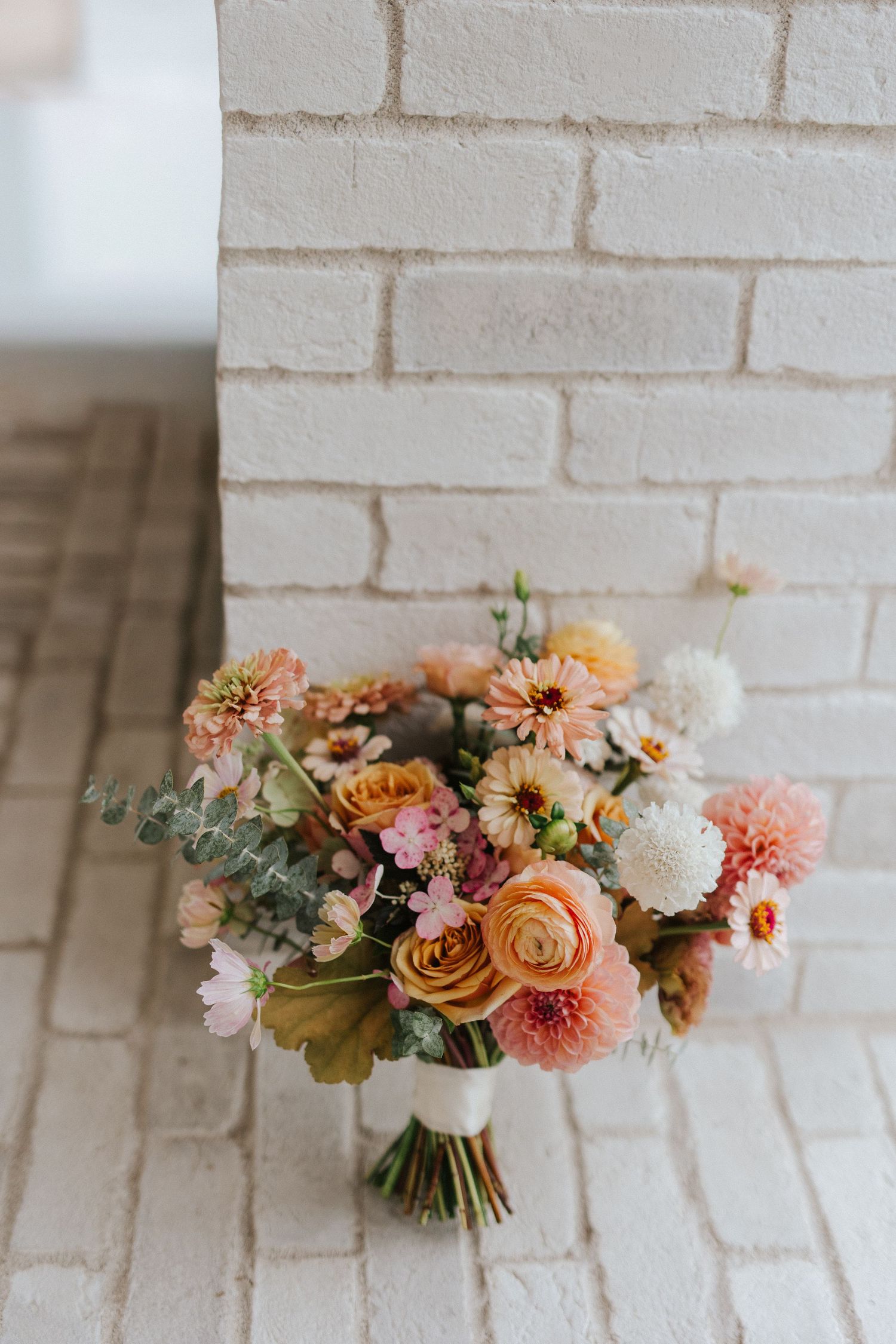 Beautiful wedding bouquet with peach dahlias, roses and eucalyptus against white brick wall in triptych style photos.