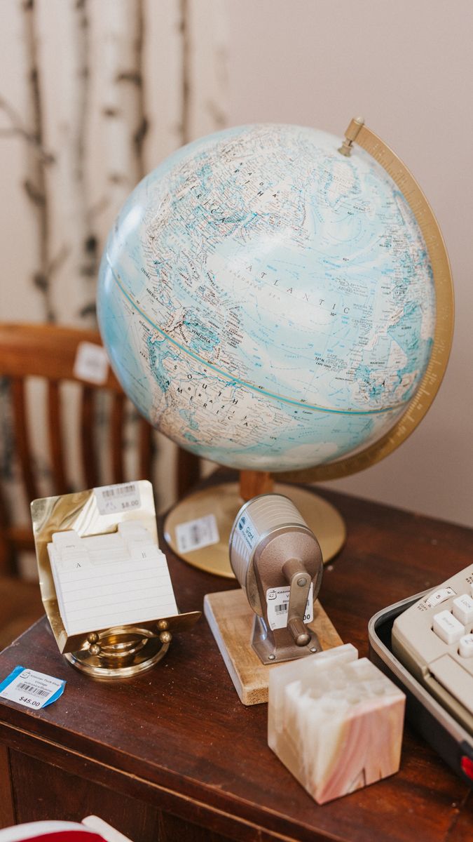 A light blue desktop globe sits on a wooden surface with various office supplies.