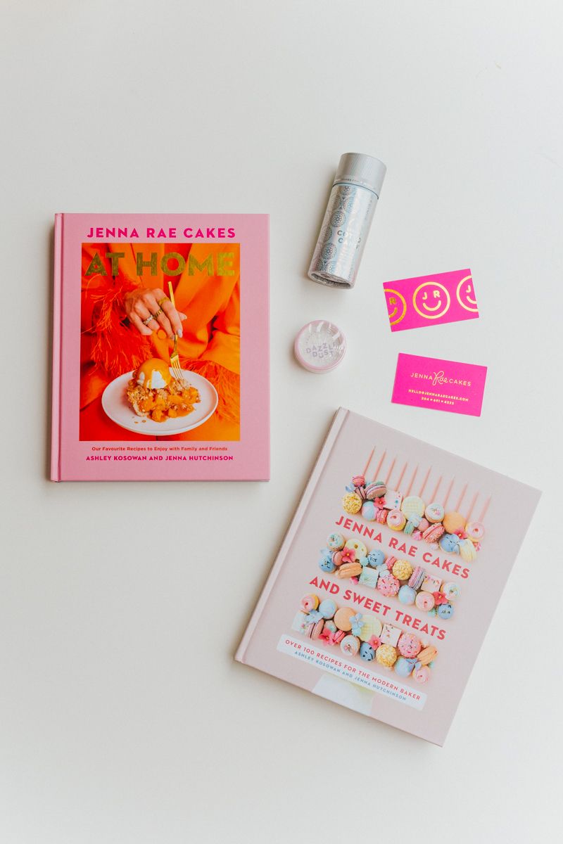 Flat lay of pink cookbooks and baking accessories on white background.