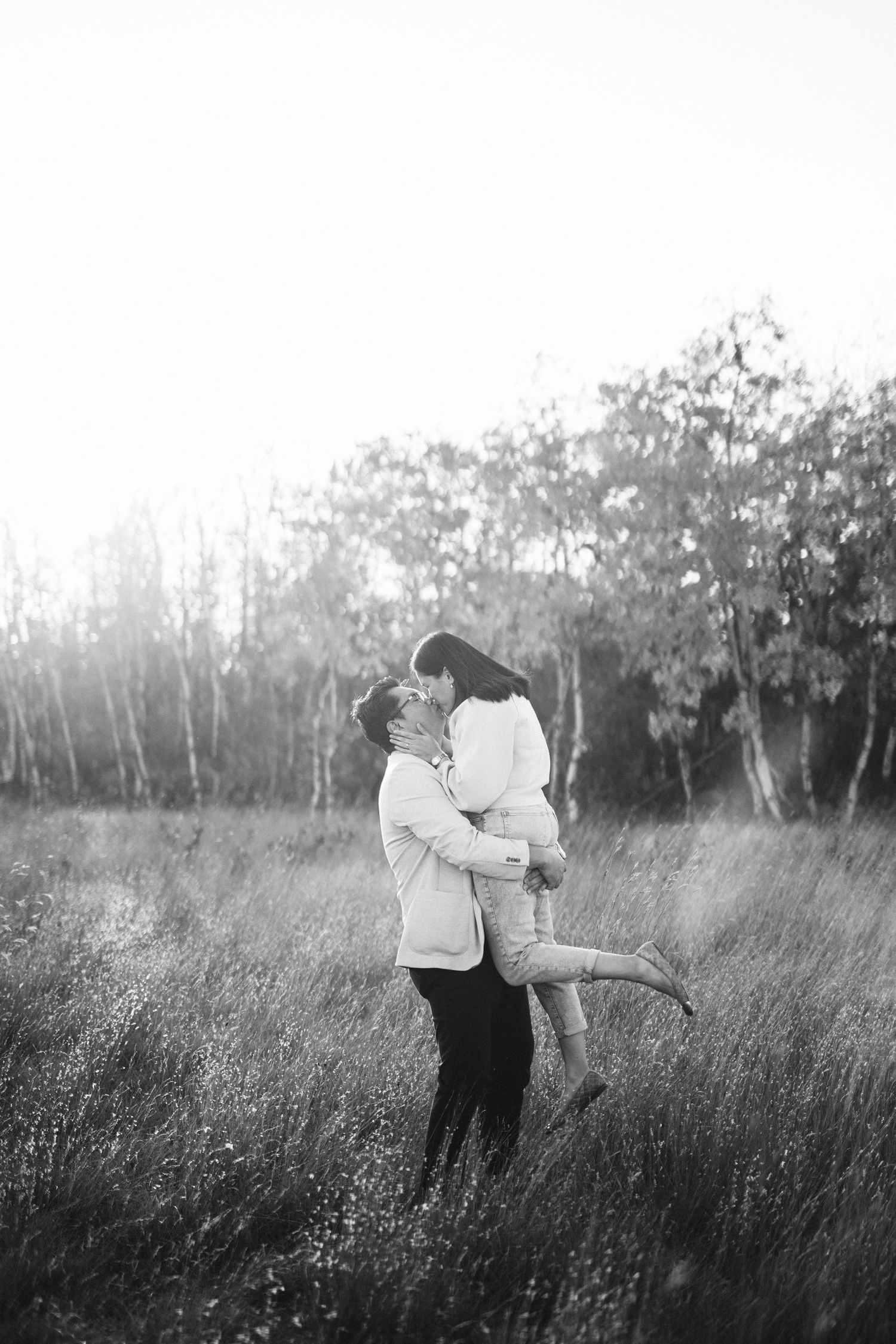 Black and white photo of couple dancing in tall grass during sunset.