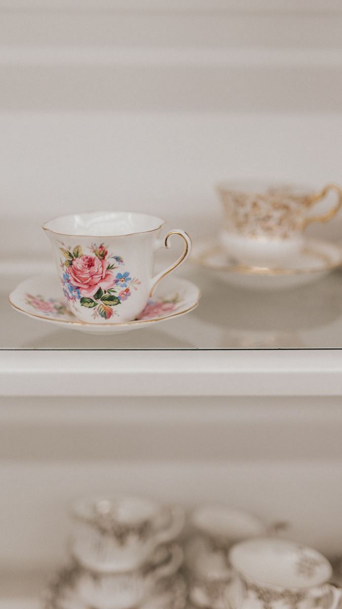 Vintage teacups with delicate floral patterns and gold trim displayed on white shelving.