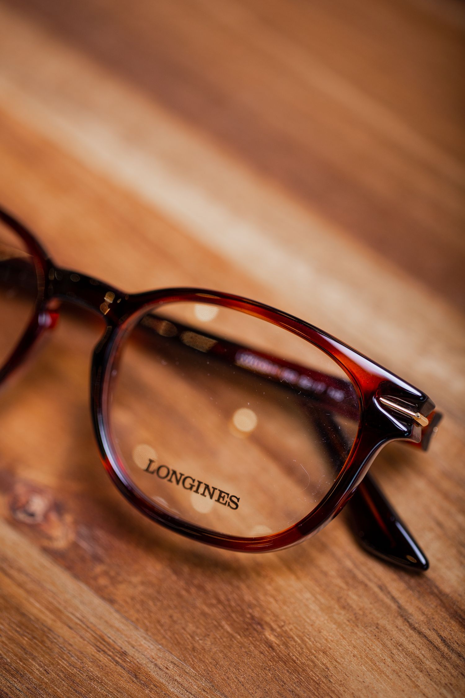 Brown Longines eyeglass frames photographed on wooden surface.