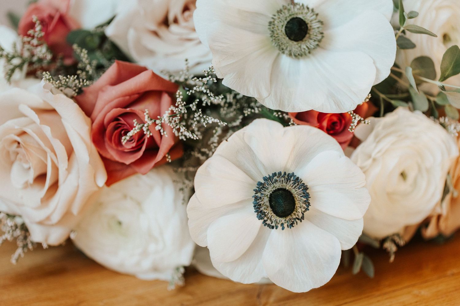 Elegant bridal bouquet with white anemone flowers and pink roses on wooden surface.