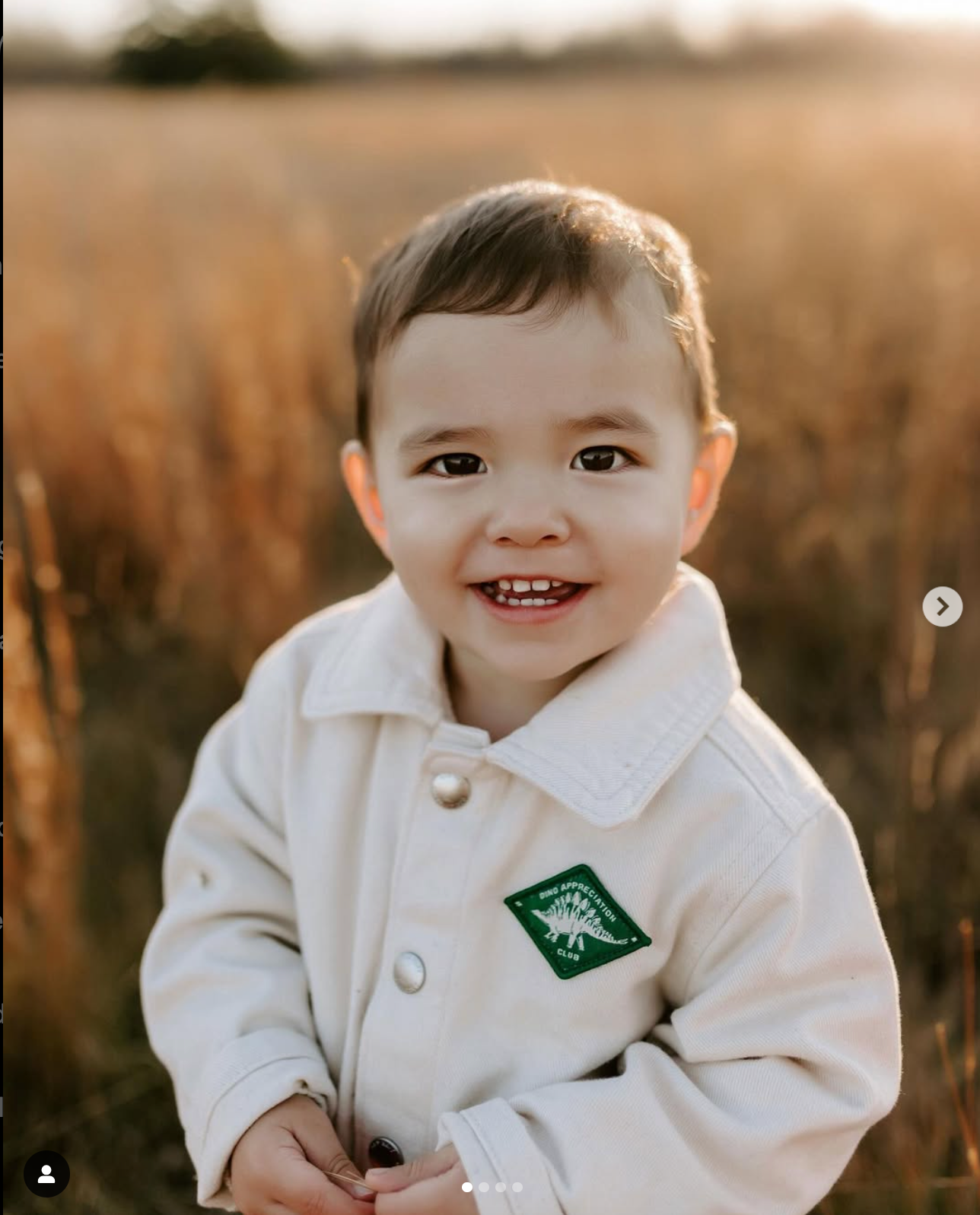 Baby wearing white collared outfit with embroidered patch smiling at camera.