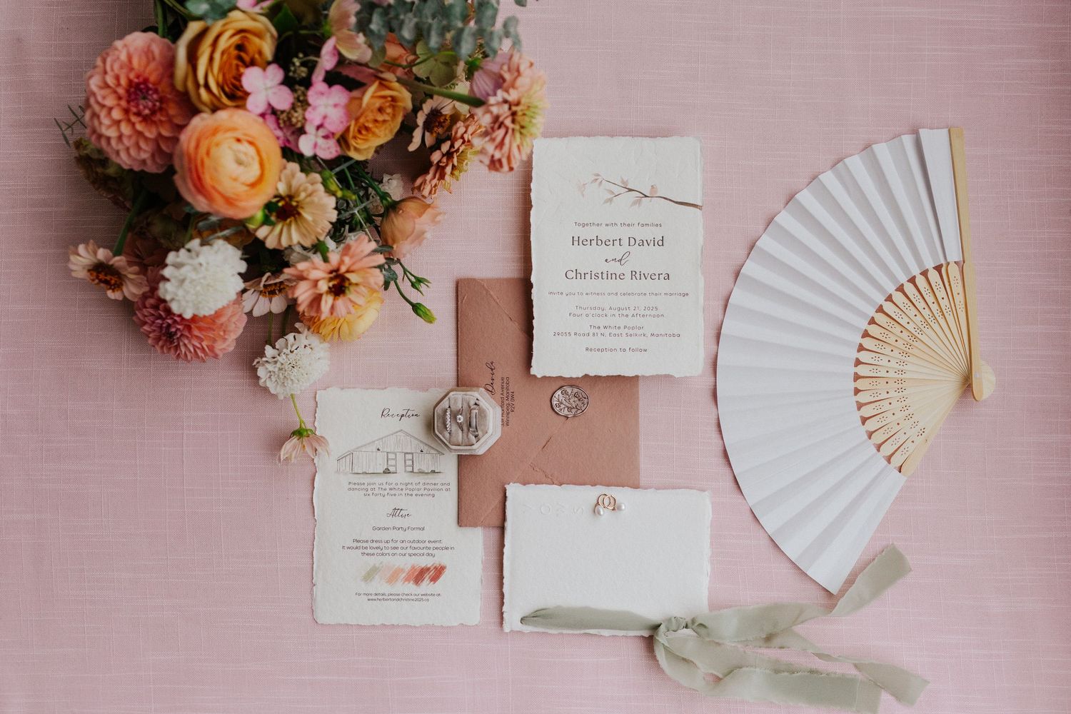 Wedding invitation suite with paper fans and floral arrangements in peach and coral tones on a pink background.