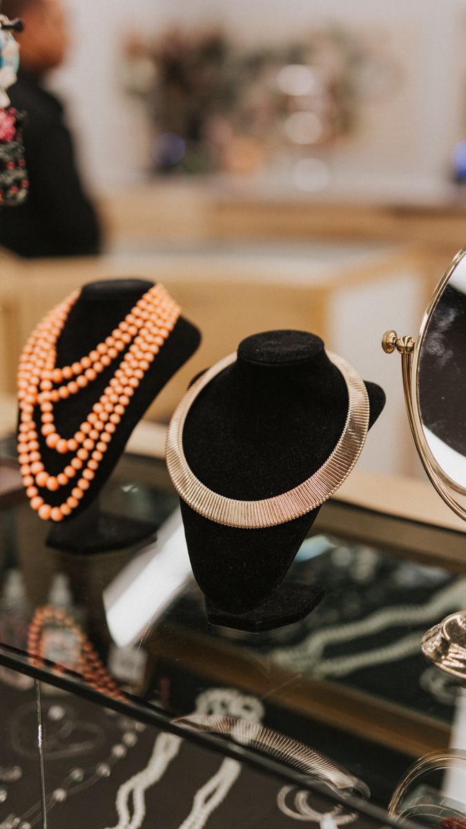 Display of elegant necklaces and jewelry on black velvet stands with coral and metallic pieces.