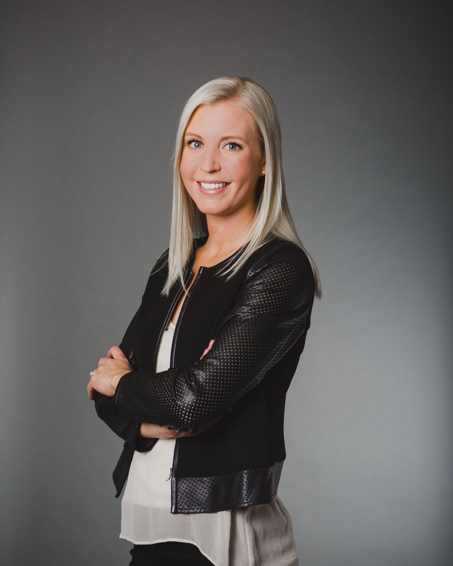 Professional studio portrait against grey background showing confident pose in black blazer.