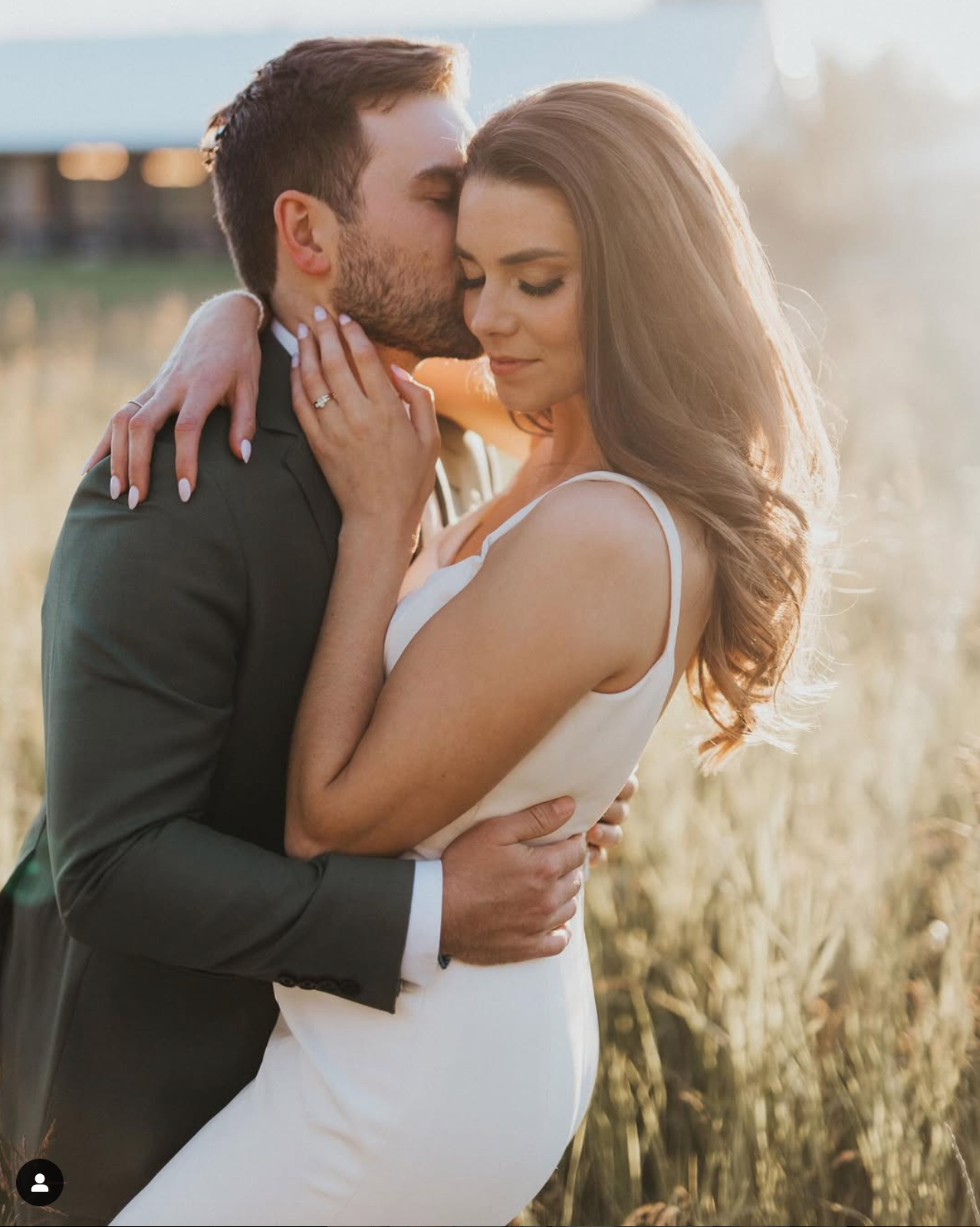 Romantic sunset moment between newlyweds in wedding attire among tall grass.