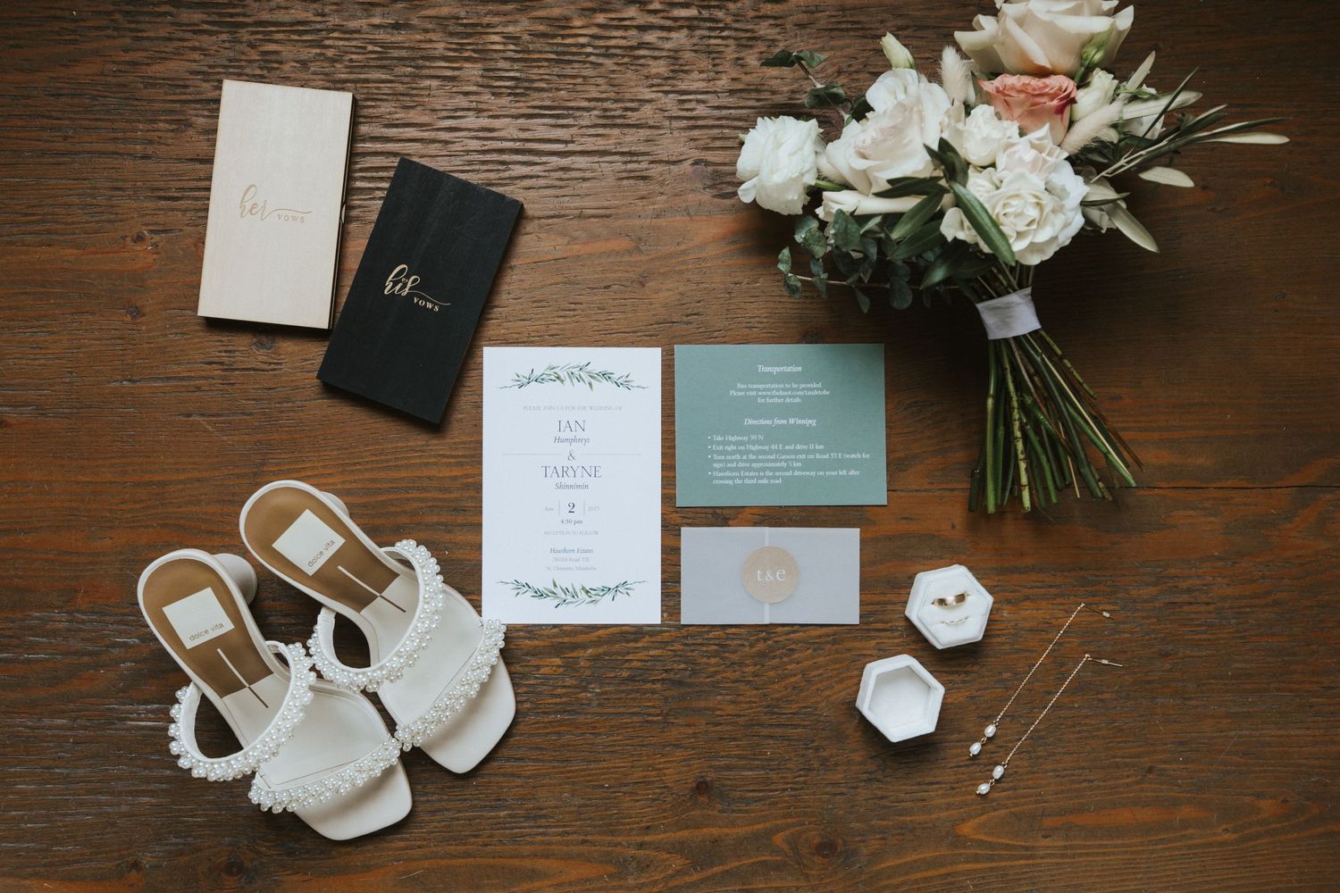 Wedding stationery and white floral arrangements elegantly displayed on dark wooden surface.