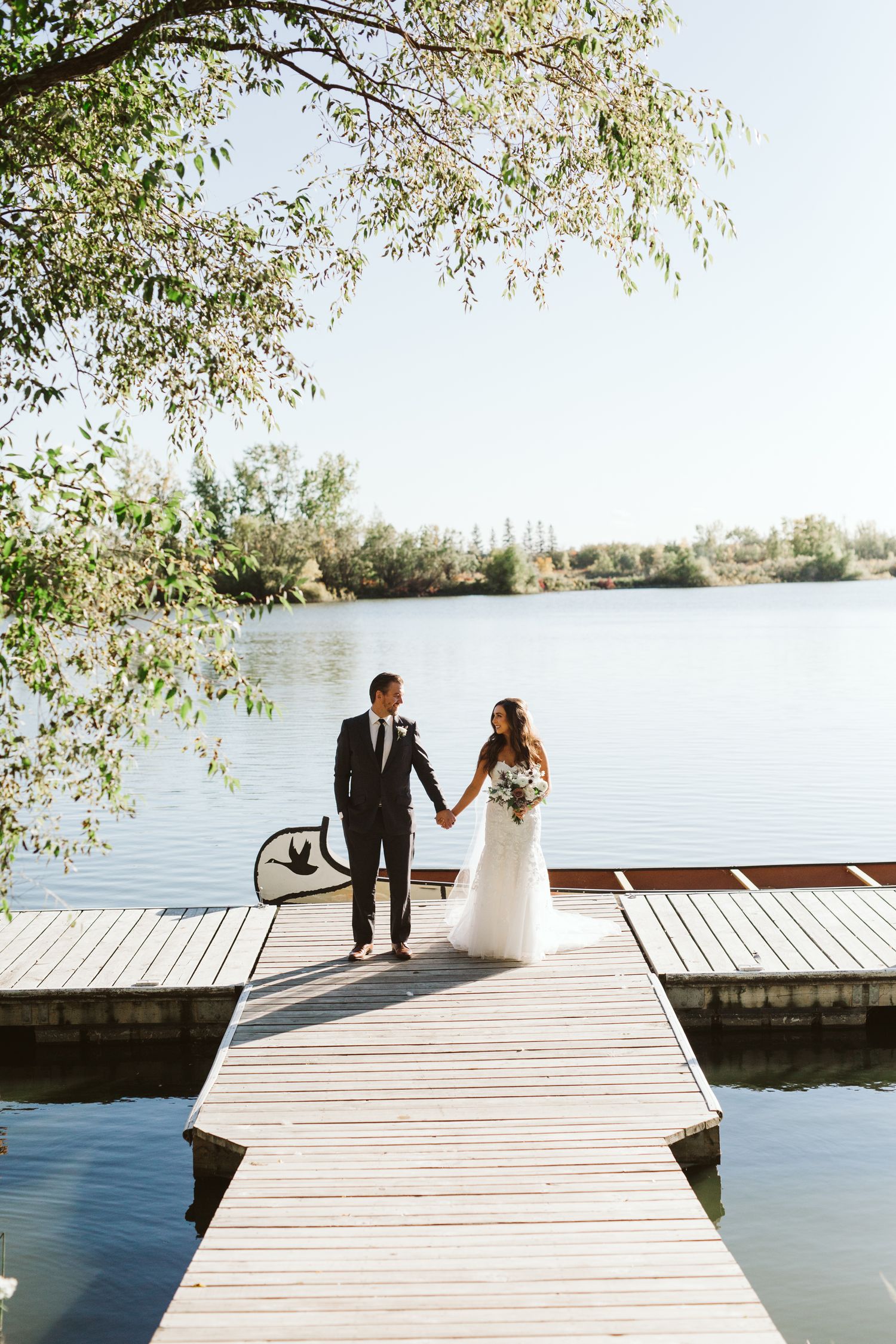 Couple standing on wooden dock overlooking serene lake on their wedding day.