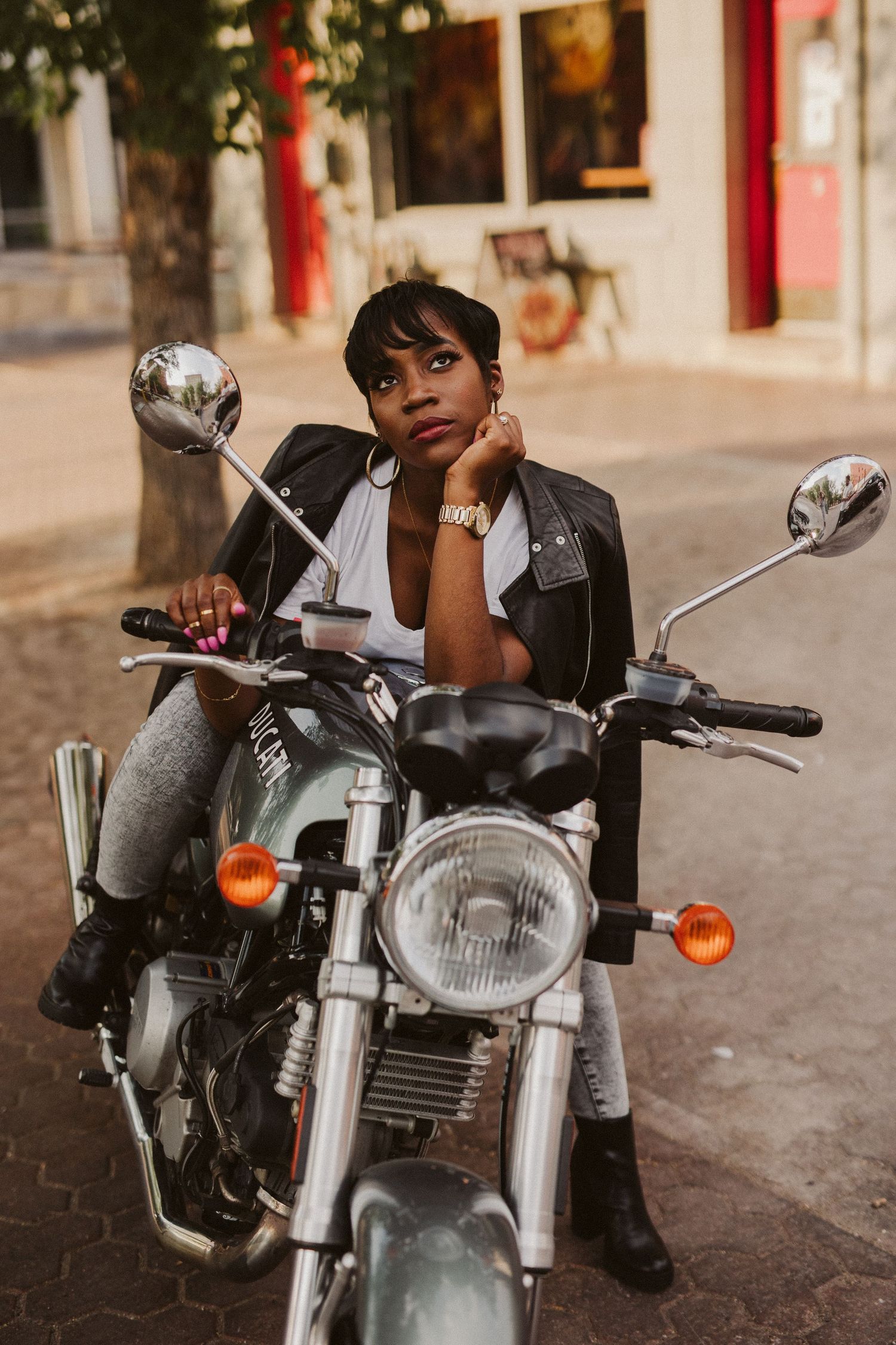 Person sitting on vintage motorcycle on cobblestone street.