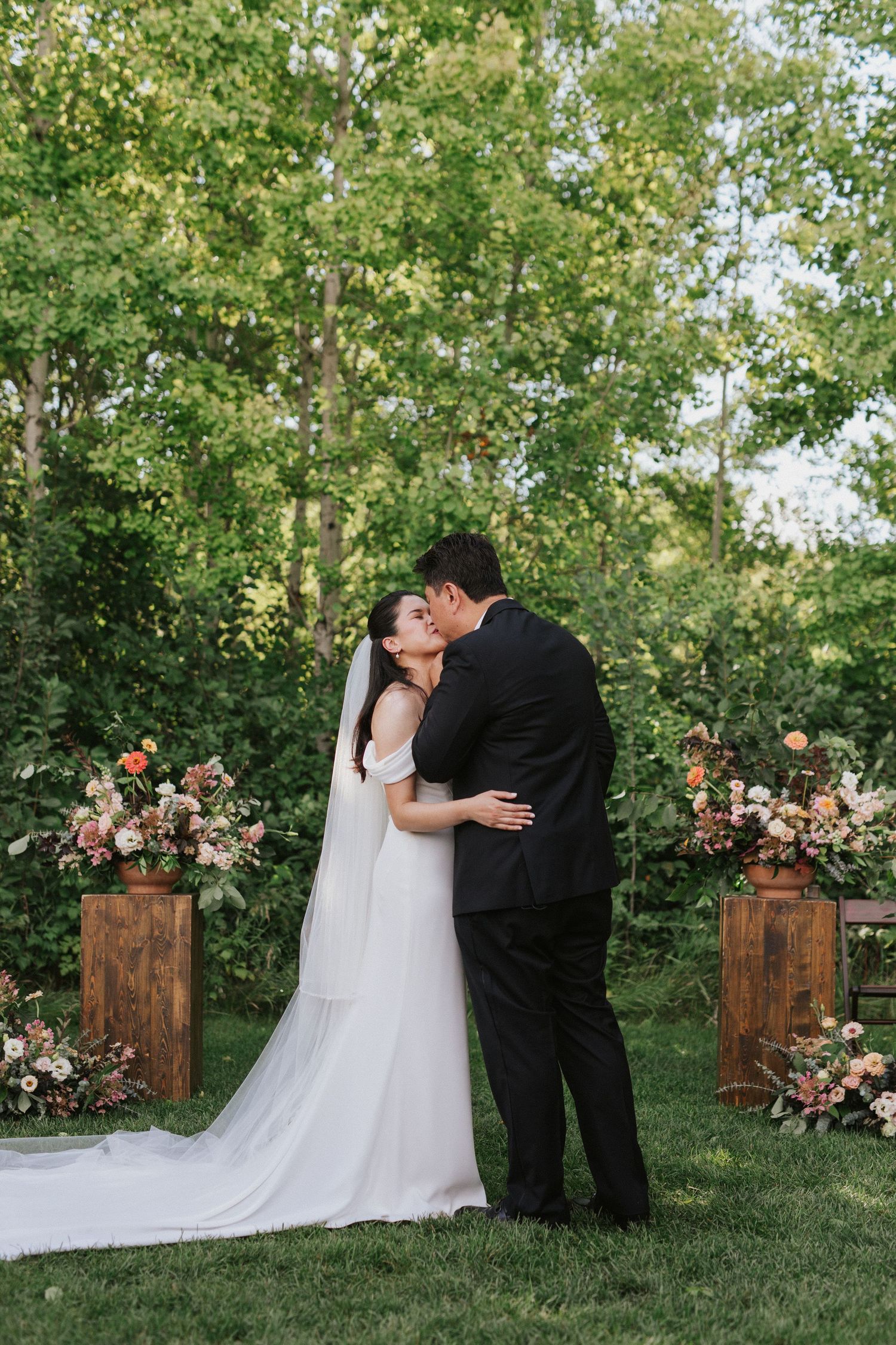 Romantic wedding couple poses for portraits in front of wooden pillars and floral arrangements.