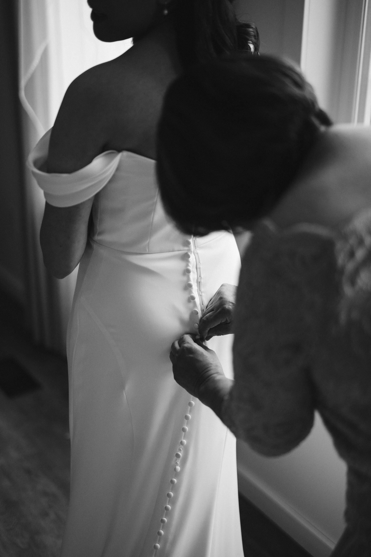 Close-up view of a white wedding dress being buttoned up, showing delicate fabric details and button closures.
