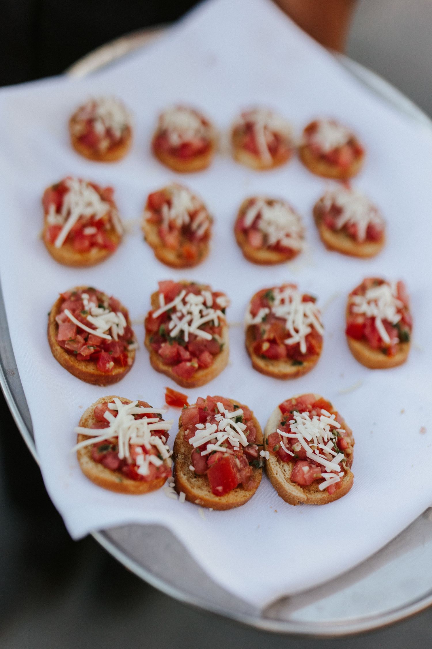 Small appetizer bites topped with tomato sauce and shredded cheese arranged on a white plate.