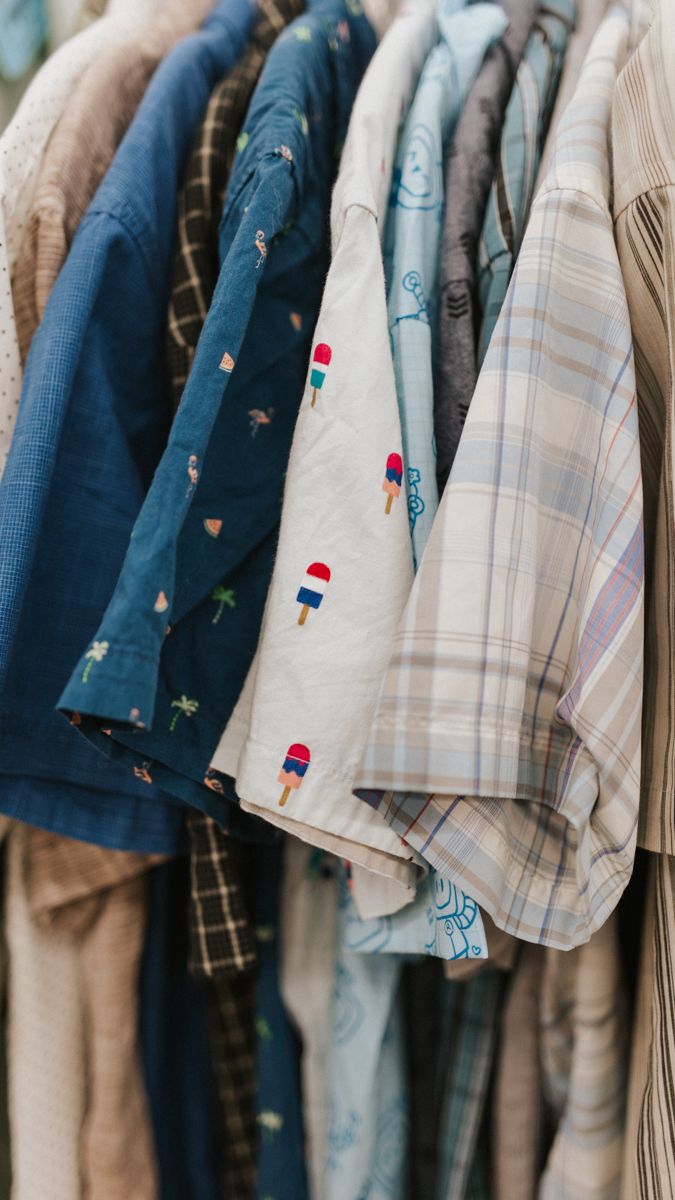 Row of casual shirts and clothing hanging on hangers in soft blue and neutral tones.