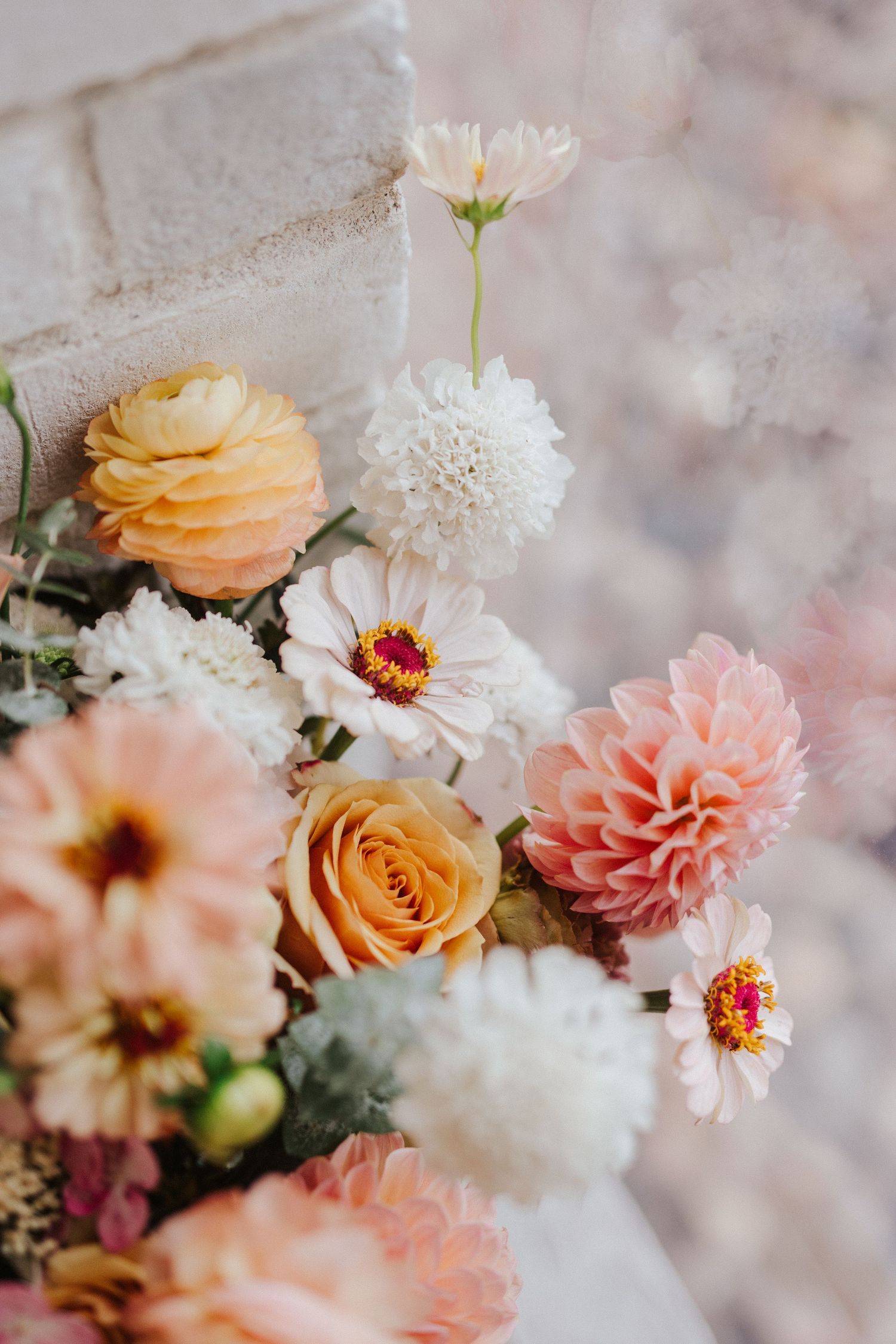 A soft pastel floral arrangement featuring peach roses, pink dahlias, and white daisies in a dreamy romantic composition.
