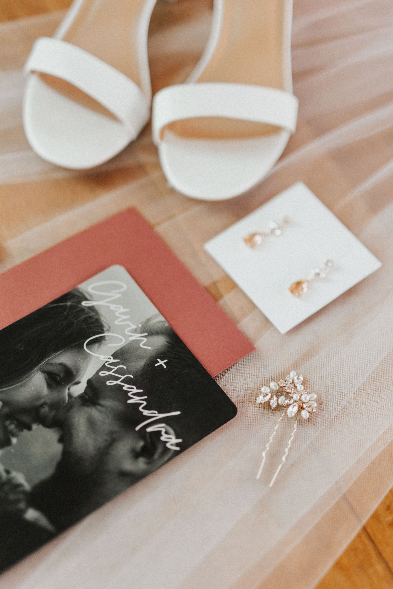 Wedding accessories including white sandals, jewelry and cards arranged on tulle fabric.