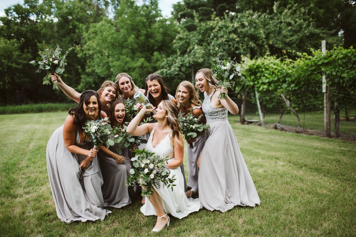 Wedding party lounges on grass enjoying candid moments during outdoor celebration.