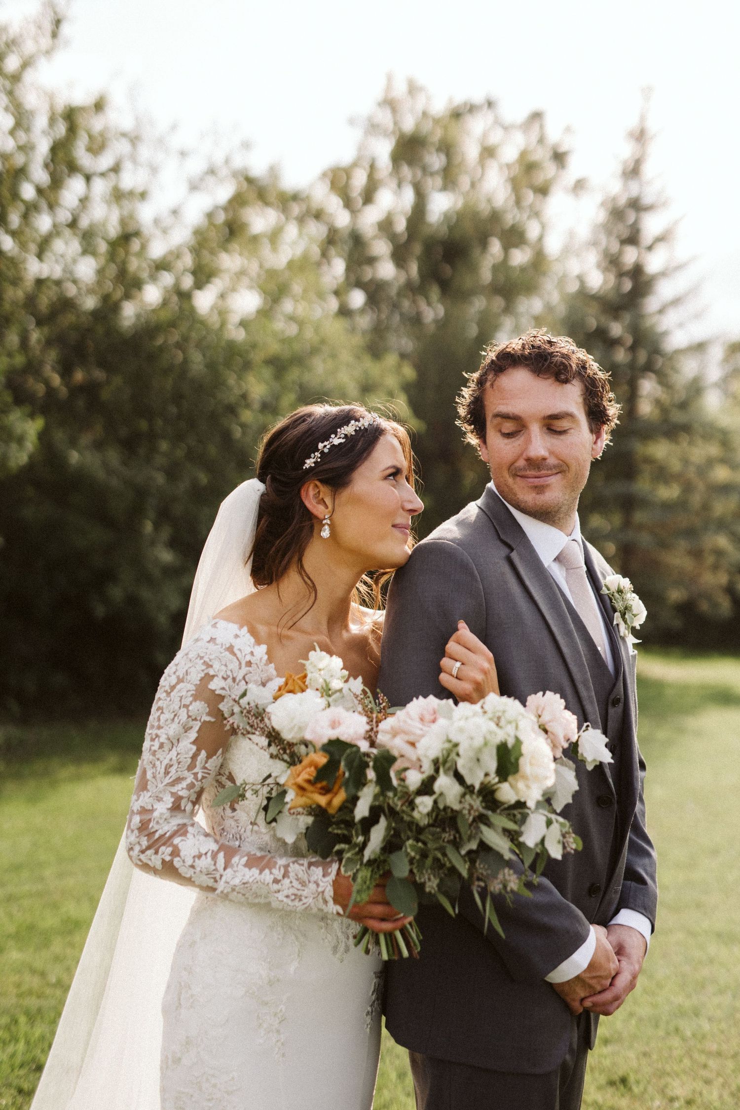 Wedding couple pose with elegant white and green bouquet in outdoor garden setting.