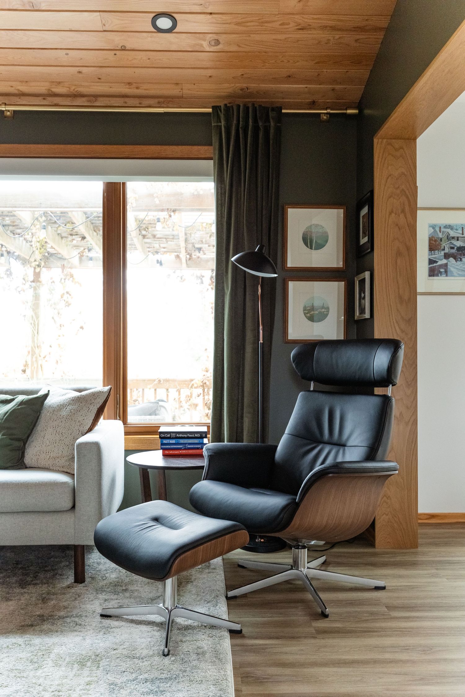 Modern lounge area featuring a leather recliner, wood-paneled ceiling, and large window with curtains.