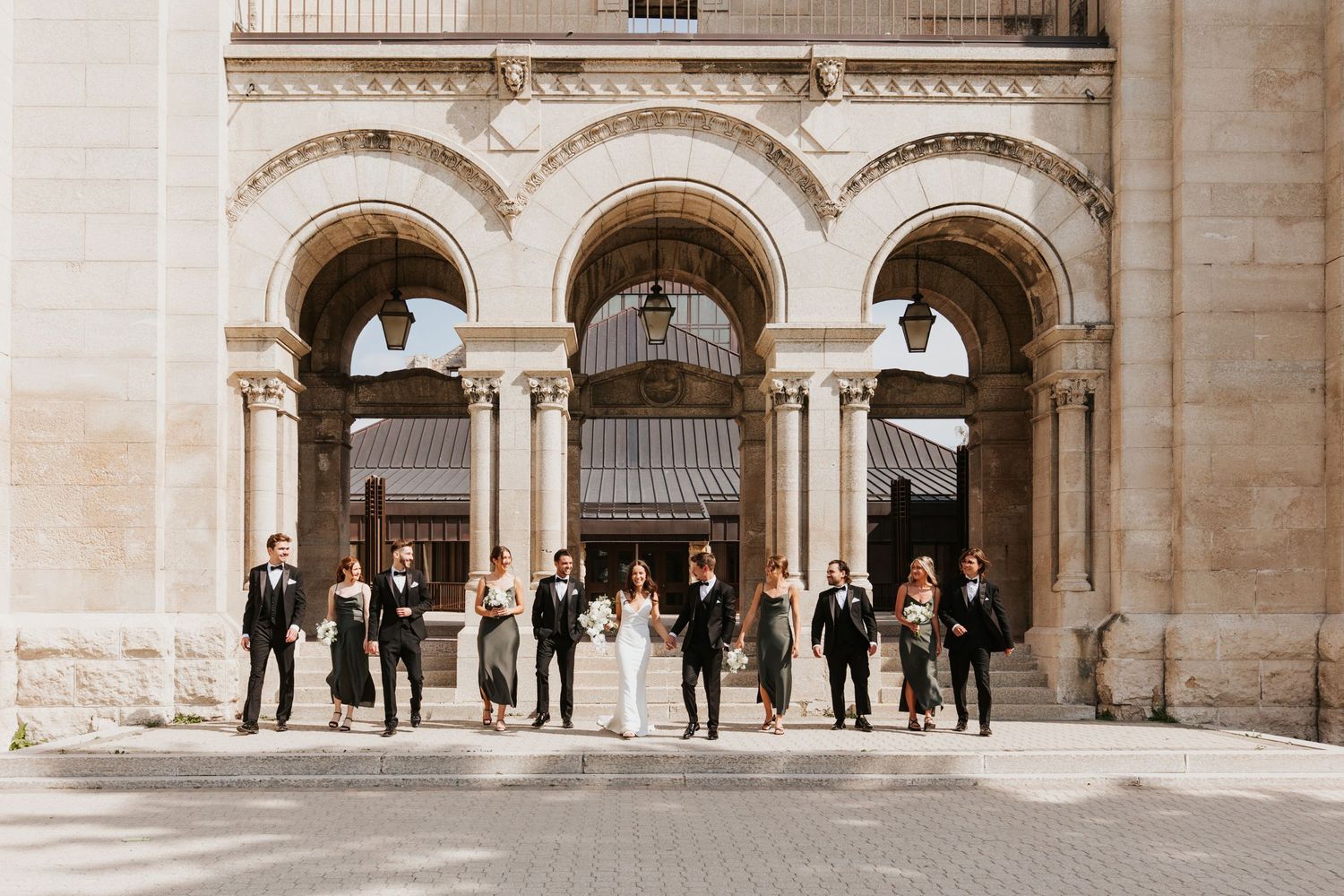Wide panoramic view of a classical stone building with arched columns and visitors.