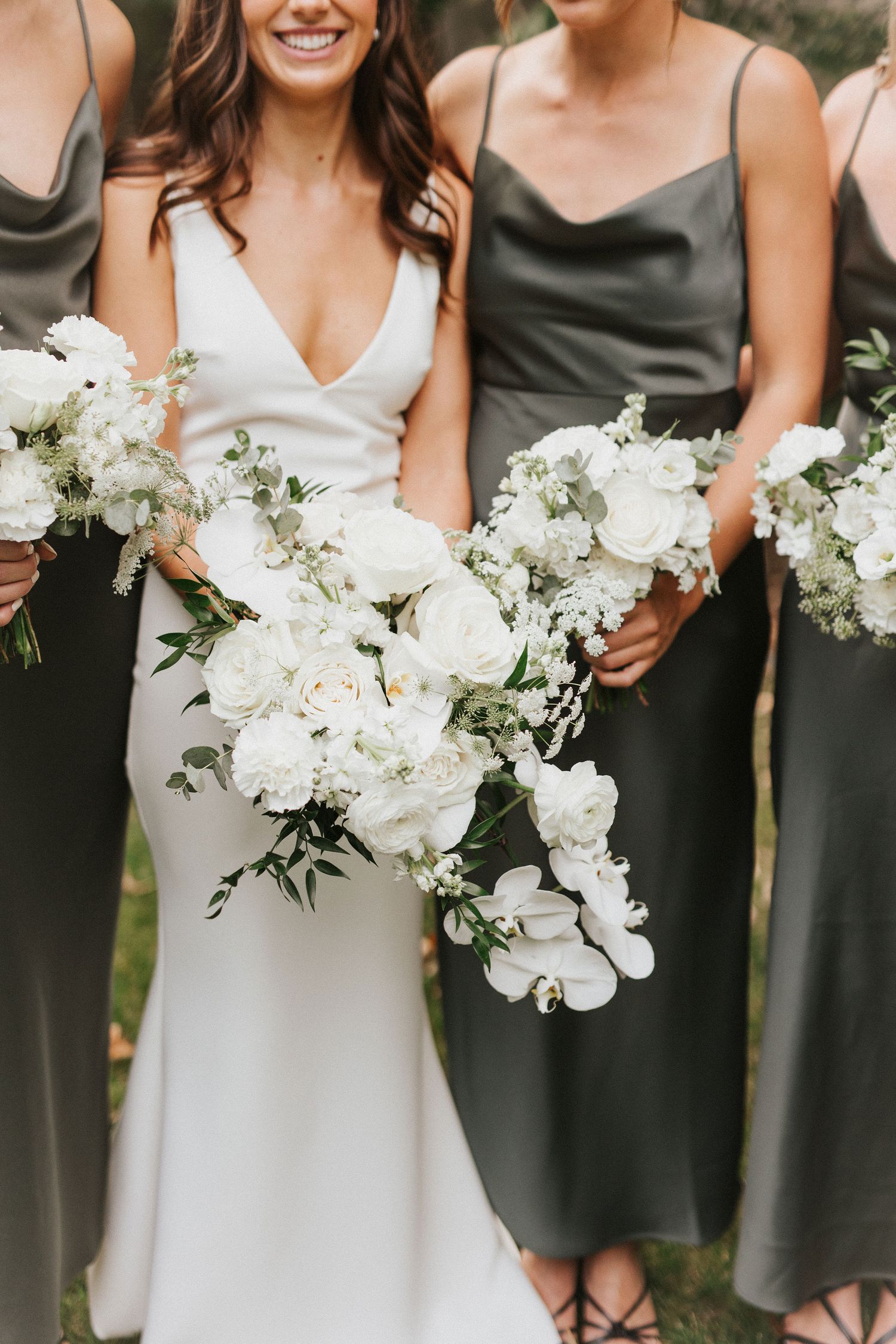 Wedding party wearing elegant white and sage green dresses holding white floral bouquets.