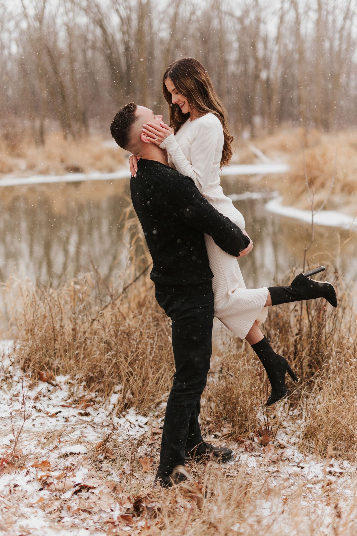 Romantic winter embrace with couple in snowy field during engagement shoot.