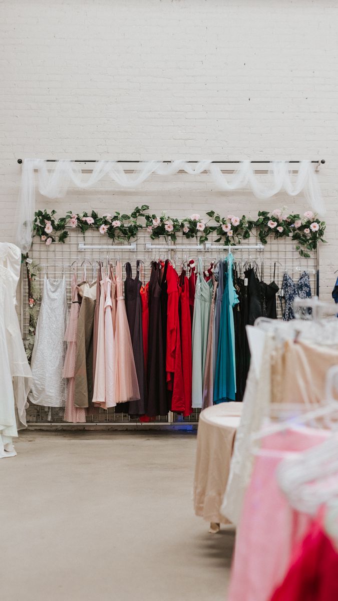 Colorful formal dresses hanging on a rack against a white wall decorated with floral garland.