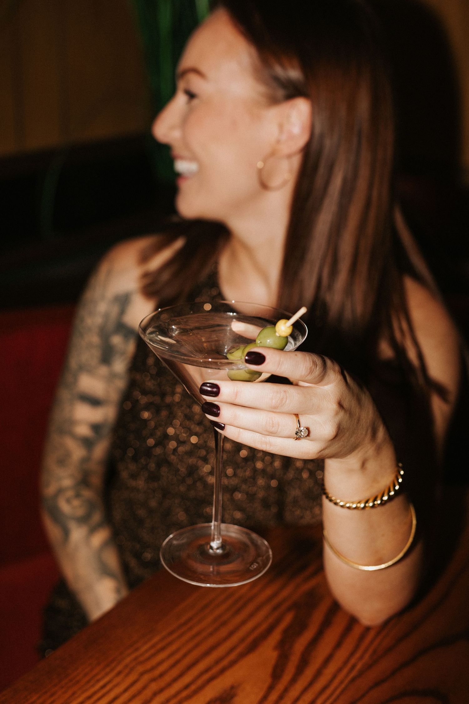 Woman in sparkly dress holding martini glass with olives at bar.