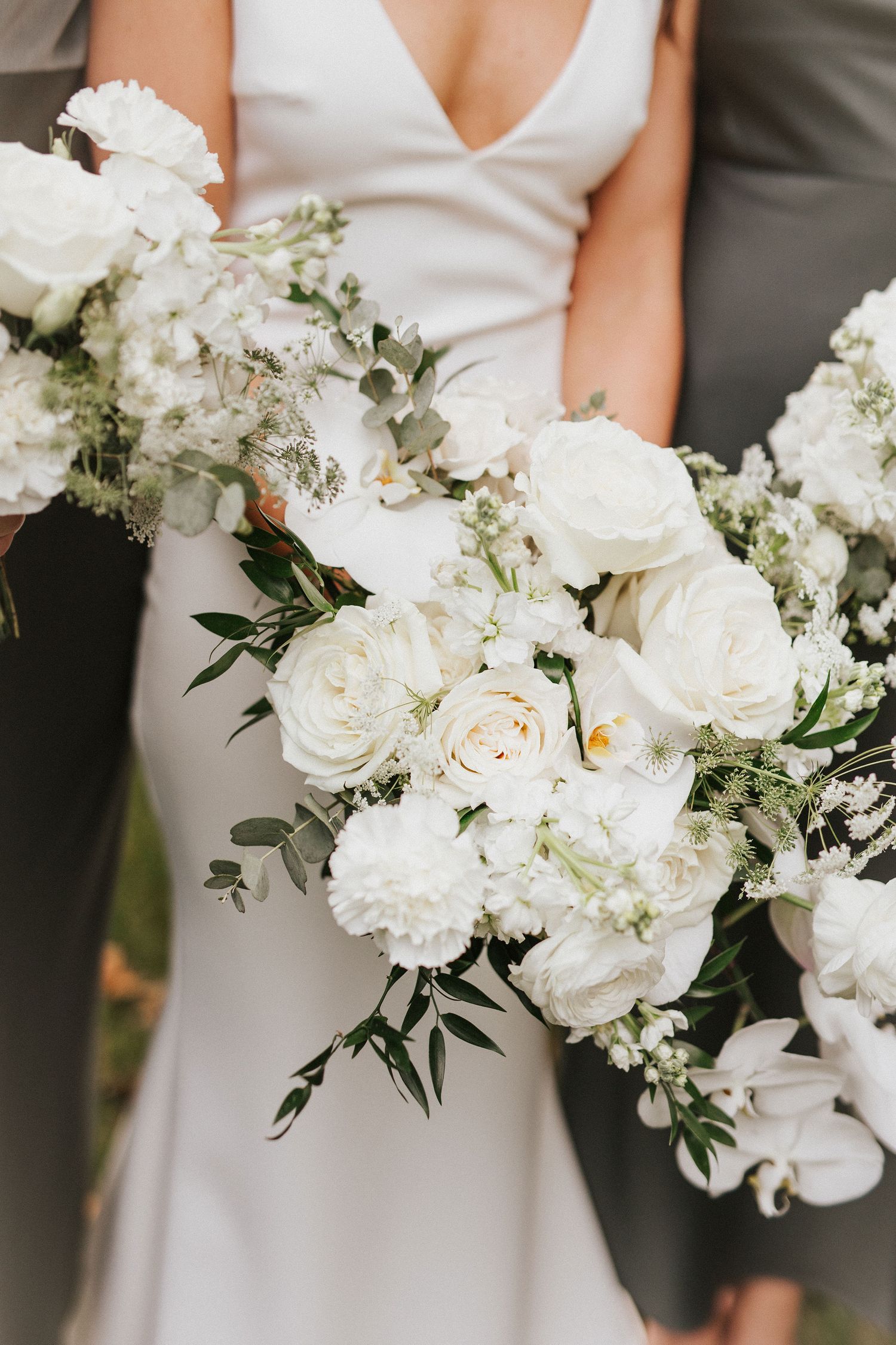 Elegant white wedding bouquets with roses and greenery held against formal attire.