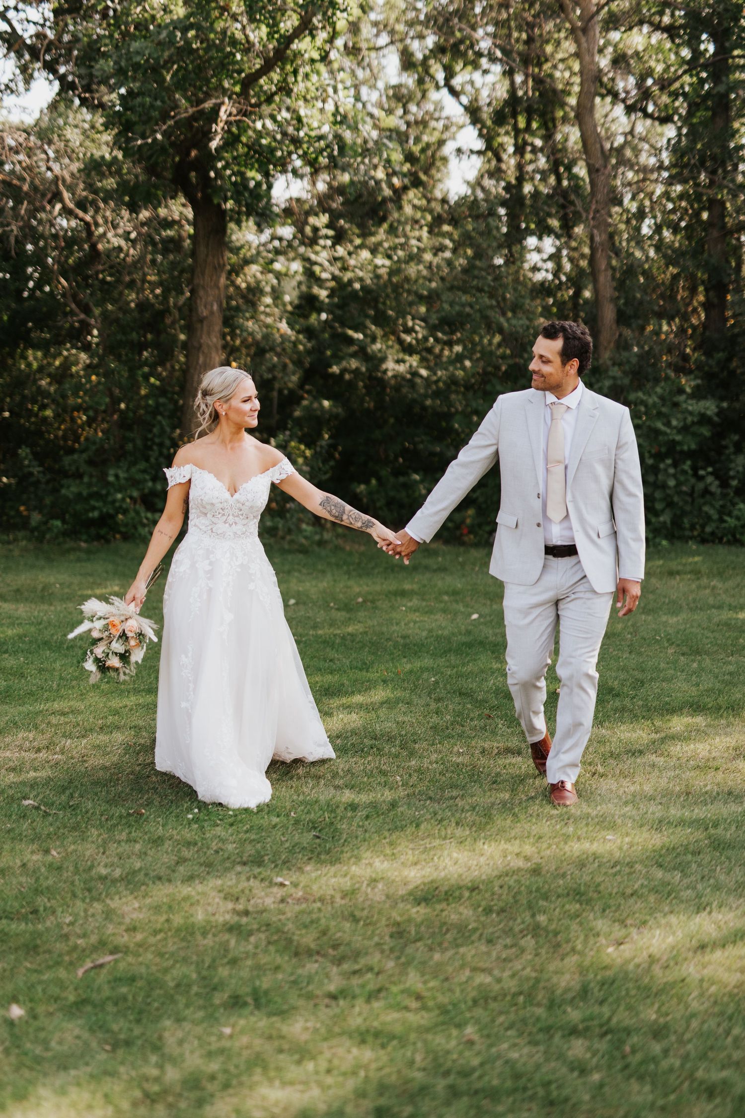 Wedding couple walking hand in hand across a sunlit garden lawn.