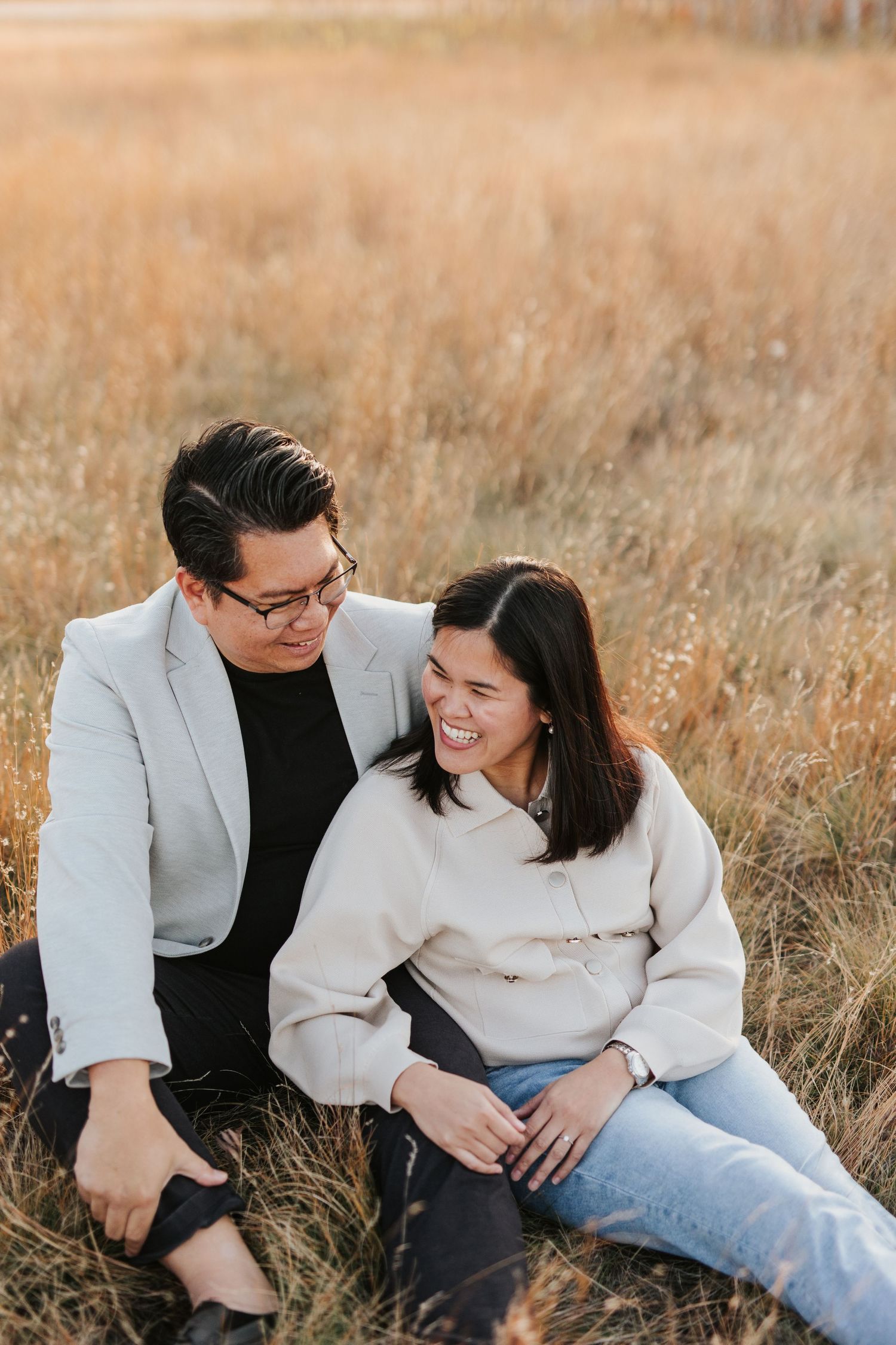 Intimate moment between couple sitting in golden field during sunset.