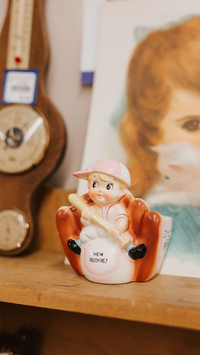 Small decorative ceramic figurine of a baby positioned on a wooden shelf.
