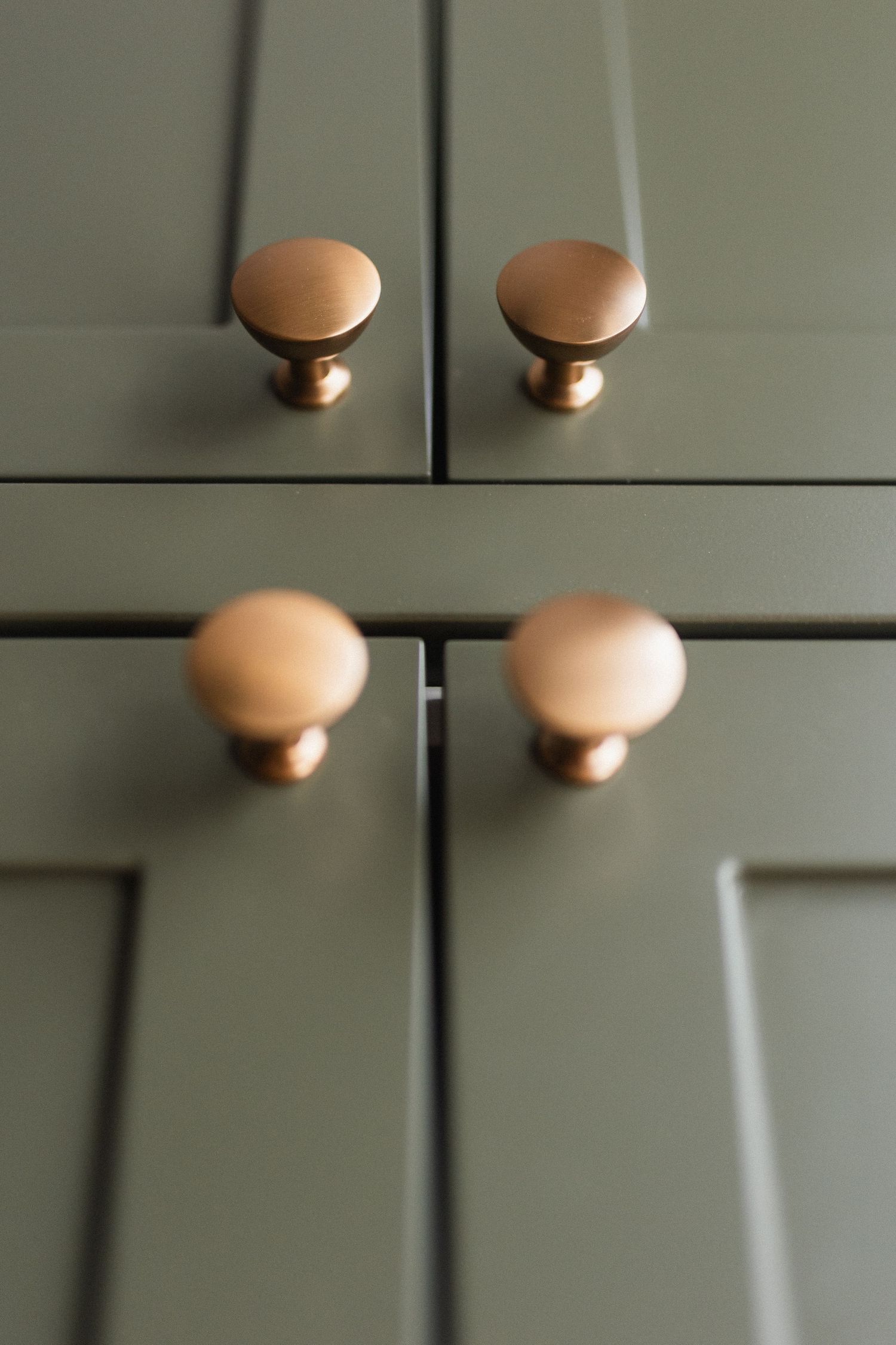 Copper-colored cabinet knobs on sage green cabinets create an elegant contrast.