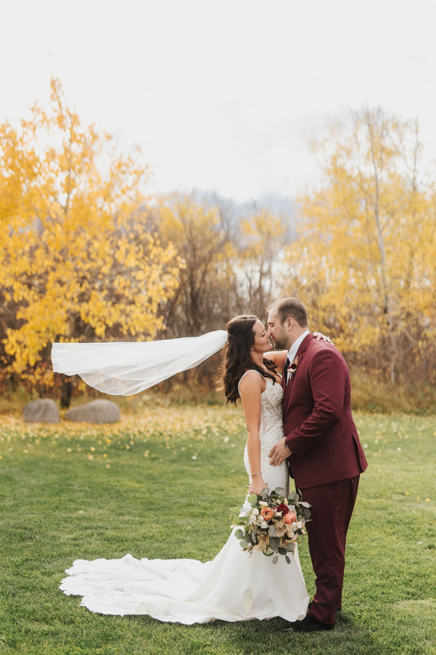 Wedding couple poses dramatically in autumn field with flowing veil.