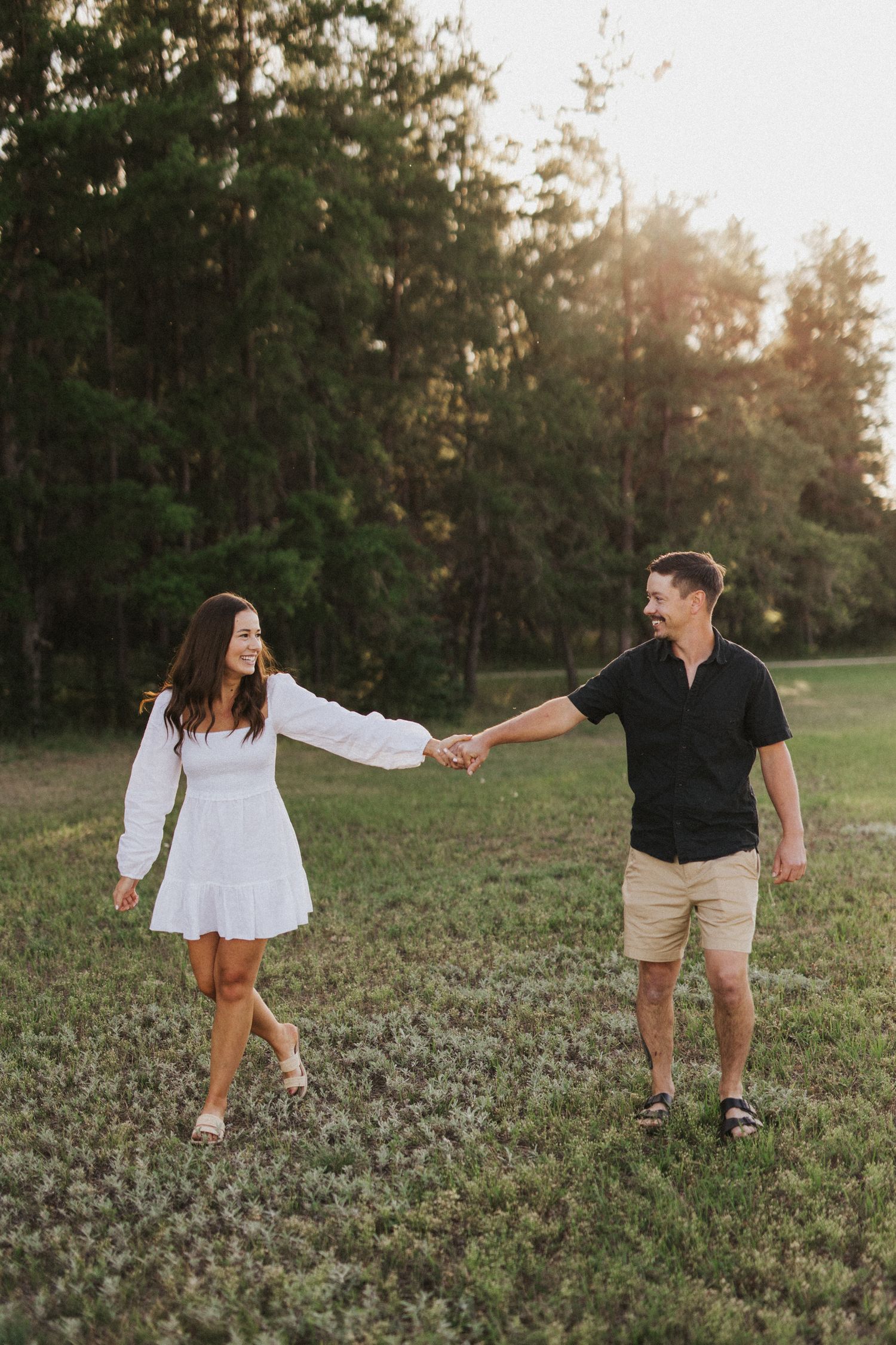 Couple dances playfully through field during sunset photo session.