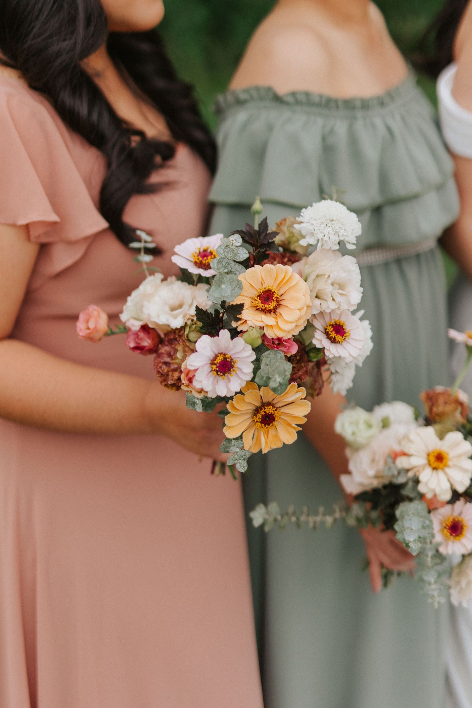 Close-up of bridesmaids holding beautiful peach and white floral bouquets with sage green accents.