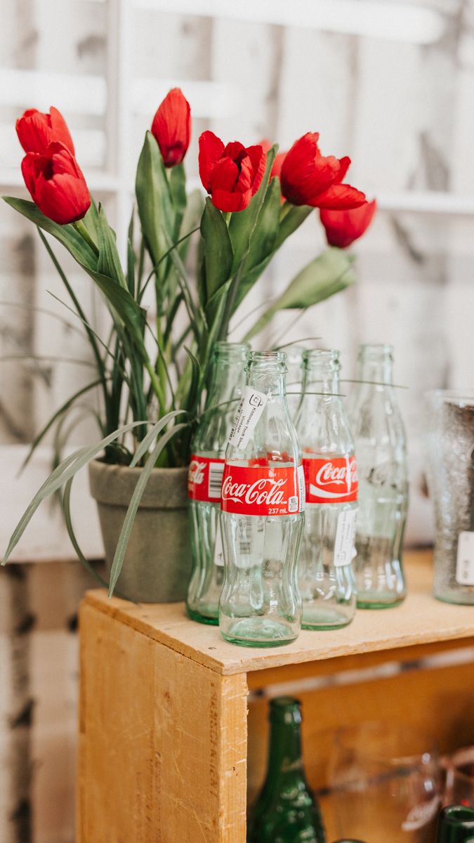 Red tulips arranged in clear Coca-Cola glass bottles on wooden surface.