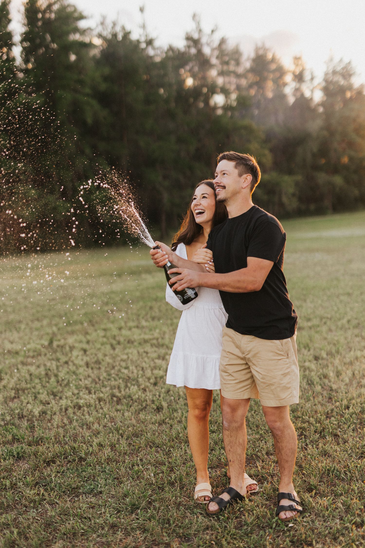 Joyful couple sprays champagne during outdoor celebration.