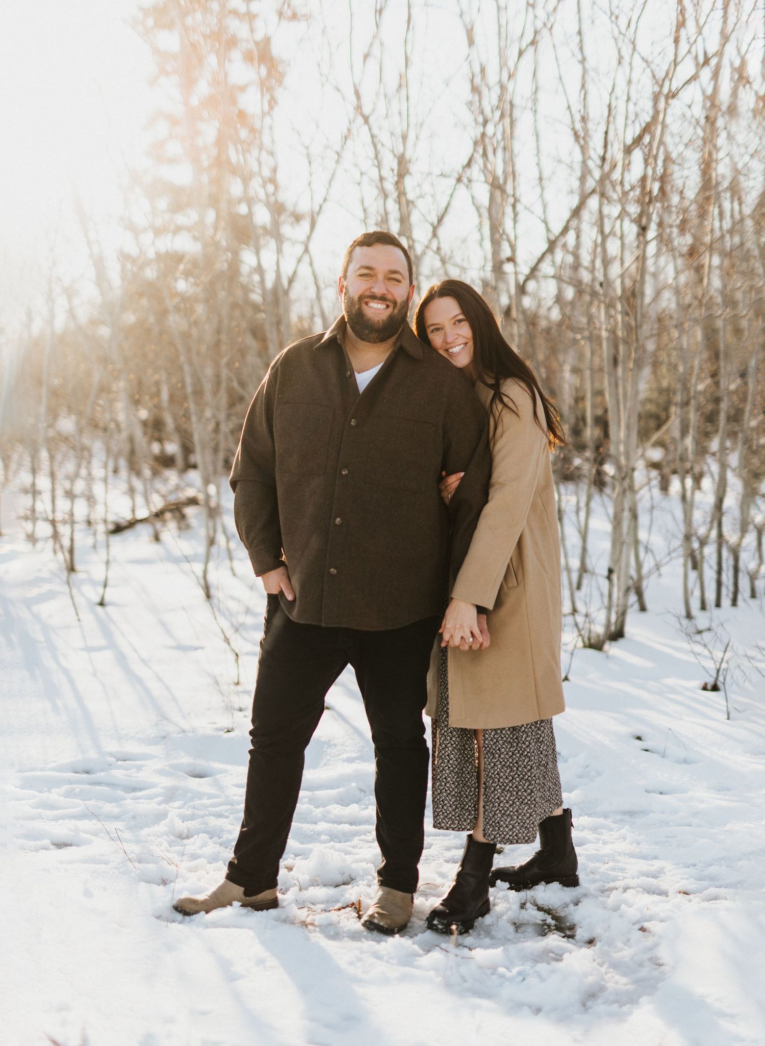 A couple poses together in a snowy winter landscape surrounded by bare trees.