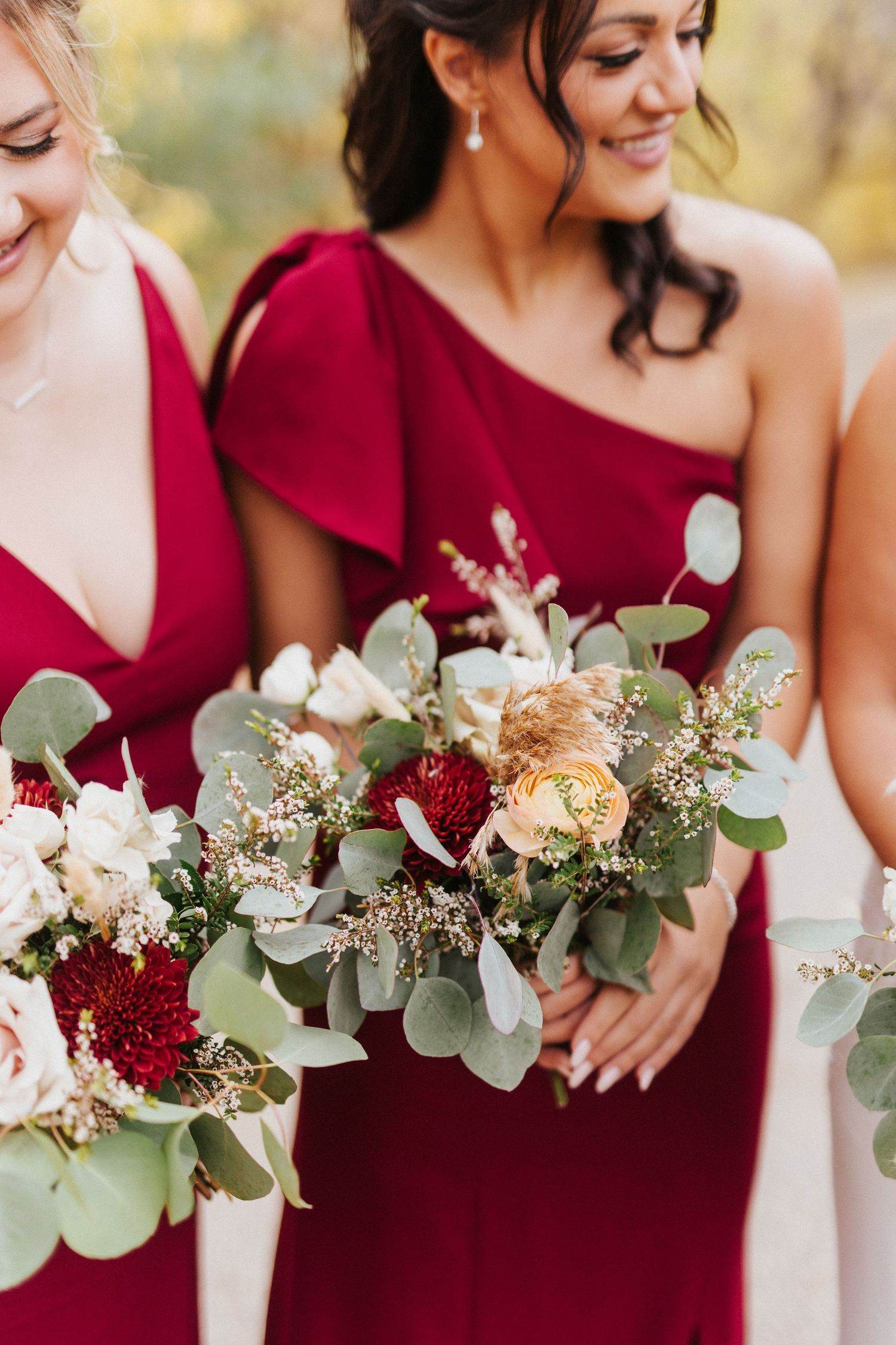 Bridesmaids in burgundy dresses holding eucalyptus and floral bouquets.