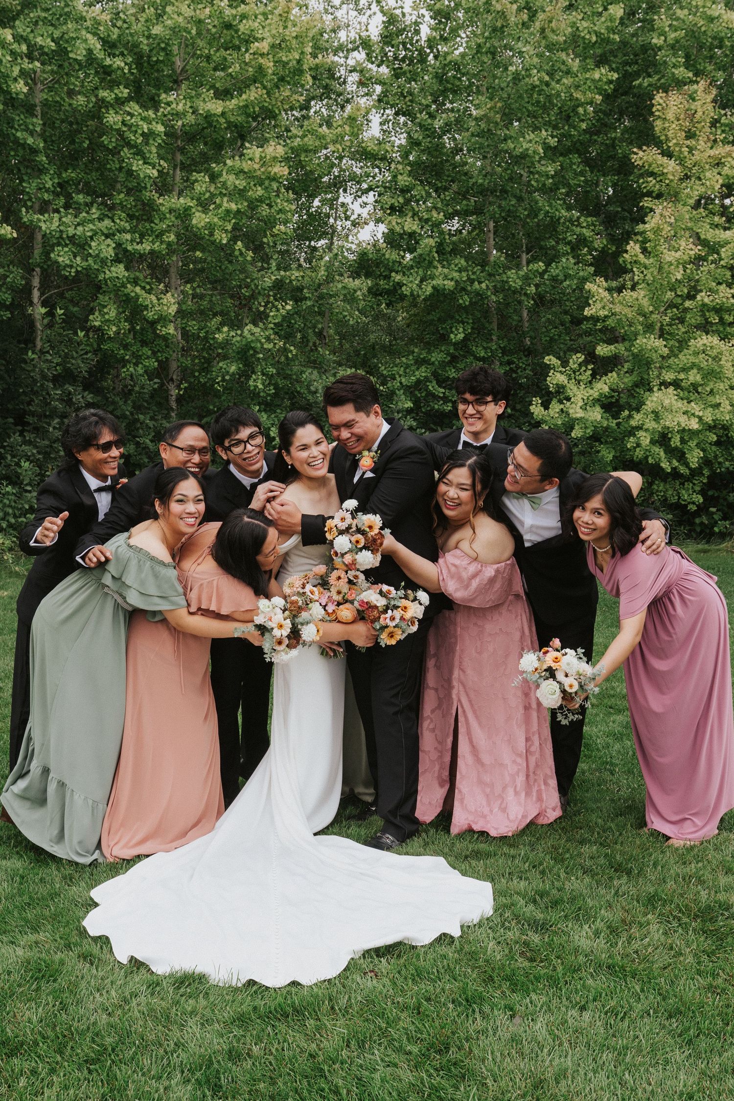 Wedding party poses for a fun group photo outdoors with colorful dresses and bouquets.