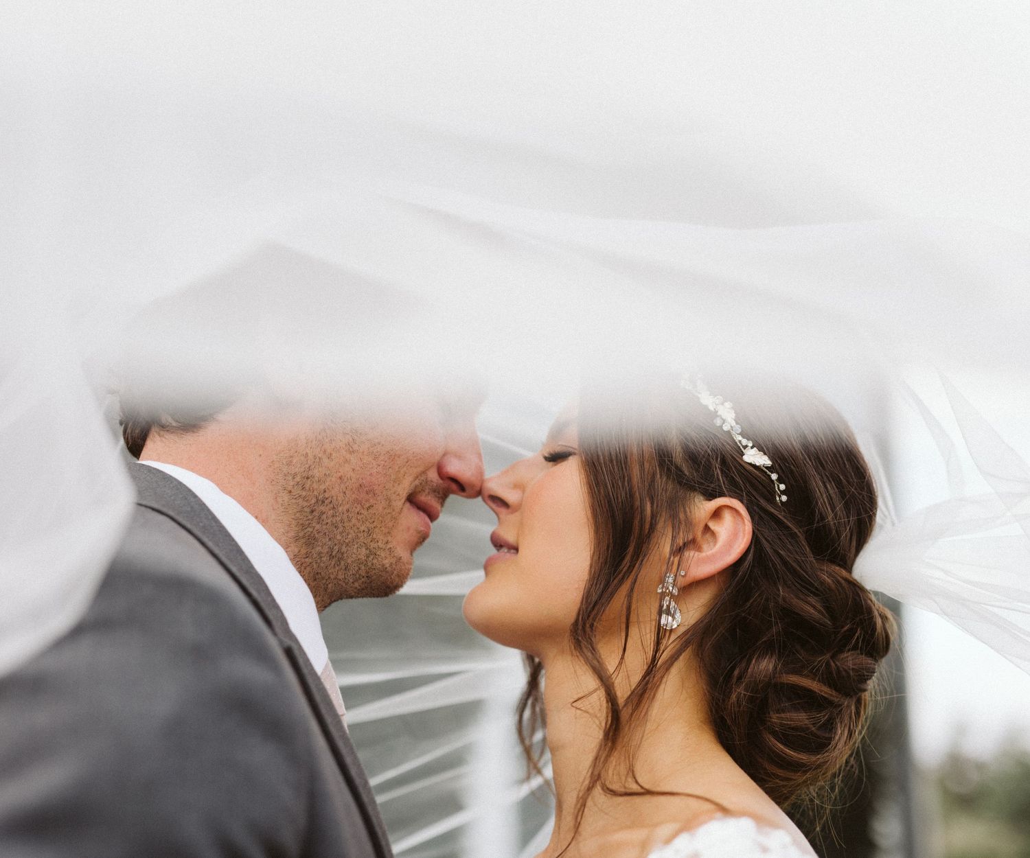 Intimate wedding moment captured under a flowing white veil against soft light.