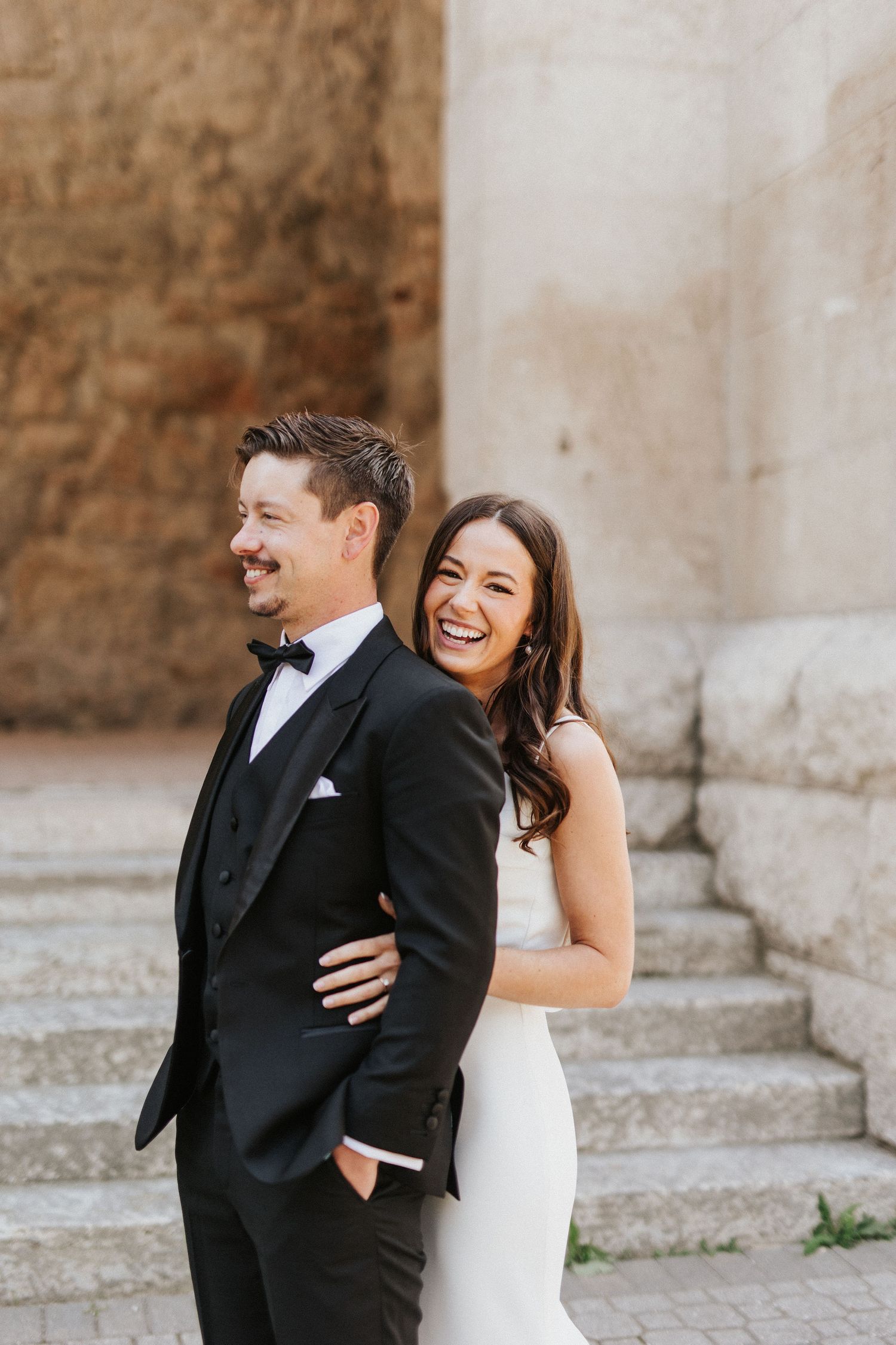 Wedding couple laughing together against a stone wall and steps.