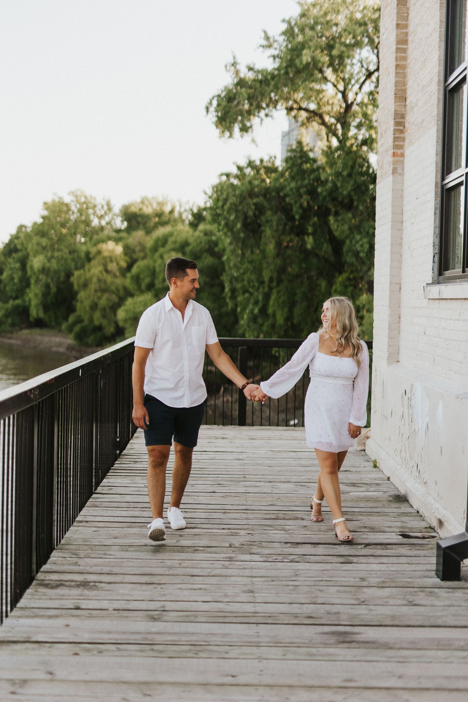 Sequence of couple walking hand-in-hand on wooden boardwalk near white building.