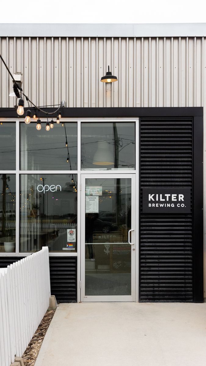 Modern storefront of Kilter Brewing Co with white and black exterior features and industrial lighting.