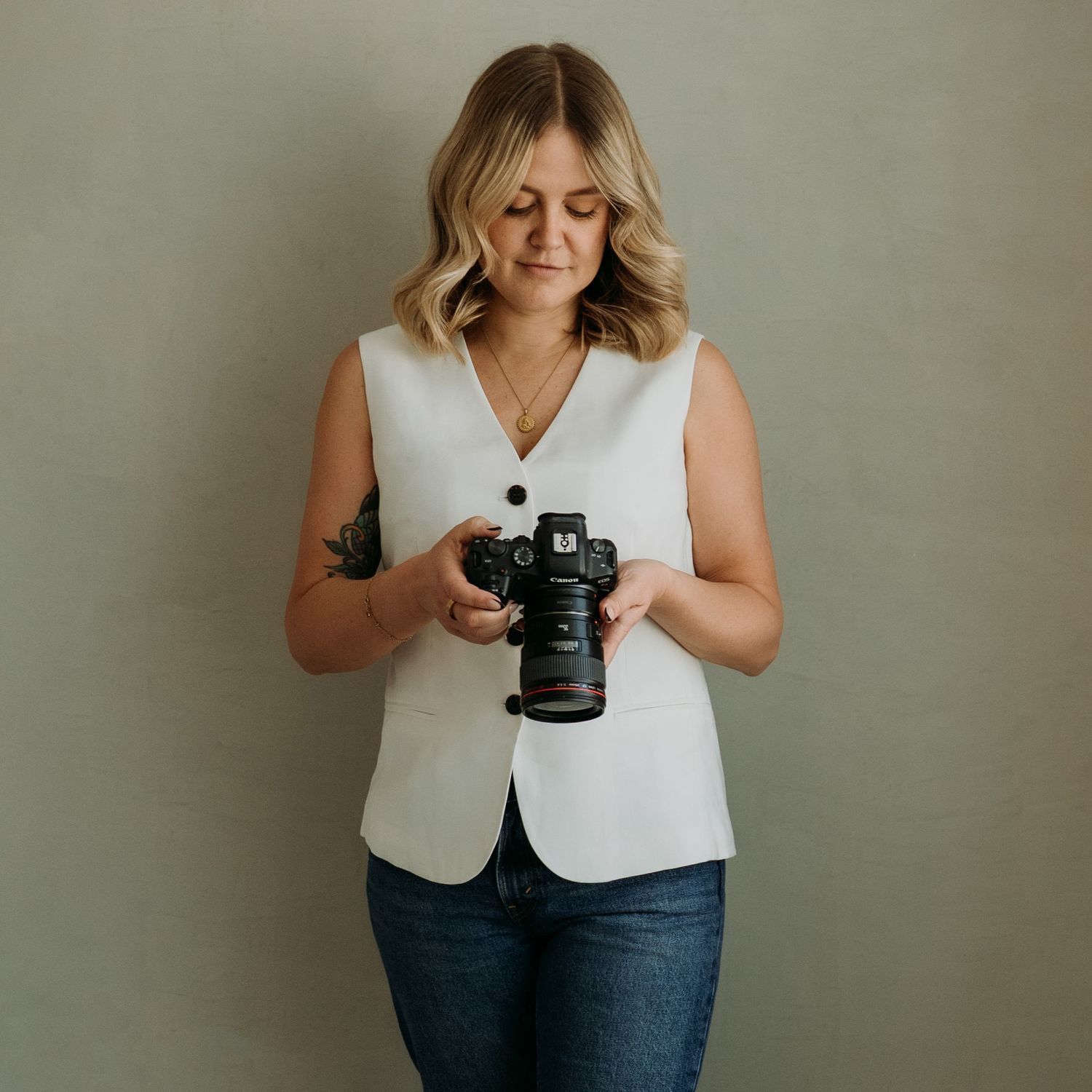Creative professional holding DSLR camera while wearing white sleeveless top and denim. Winnipeg Wedding Photographer. Aly Tam Photography.