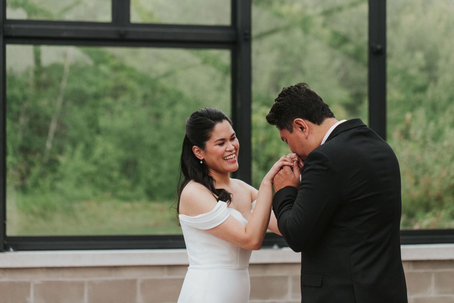 Couple dancing together during their first dance at a wedding reception with large windows in background.