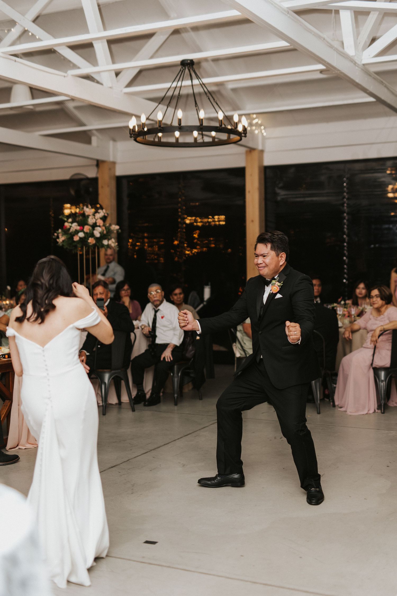 A couple dancing at their wedding reception under a rustic chandelier in an elegant venue.